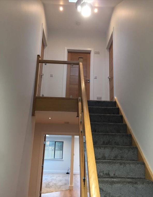 Carpeted staircase with oak strings, newel posts and glass balustrade in a finished hallway
