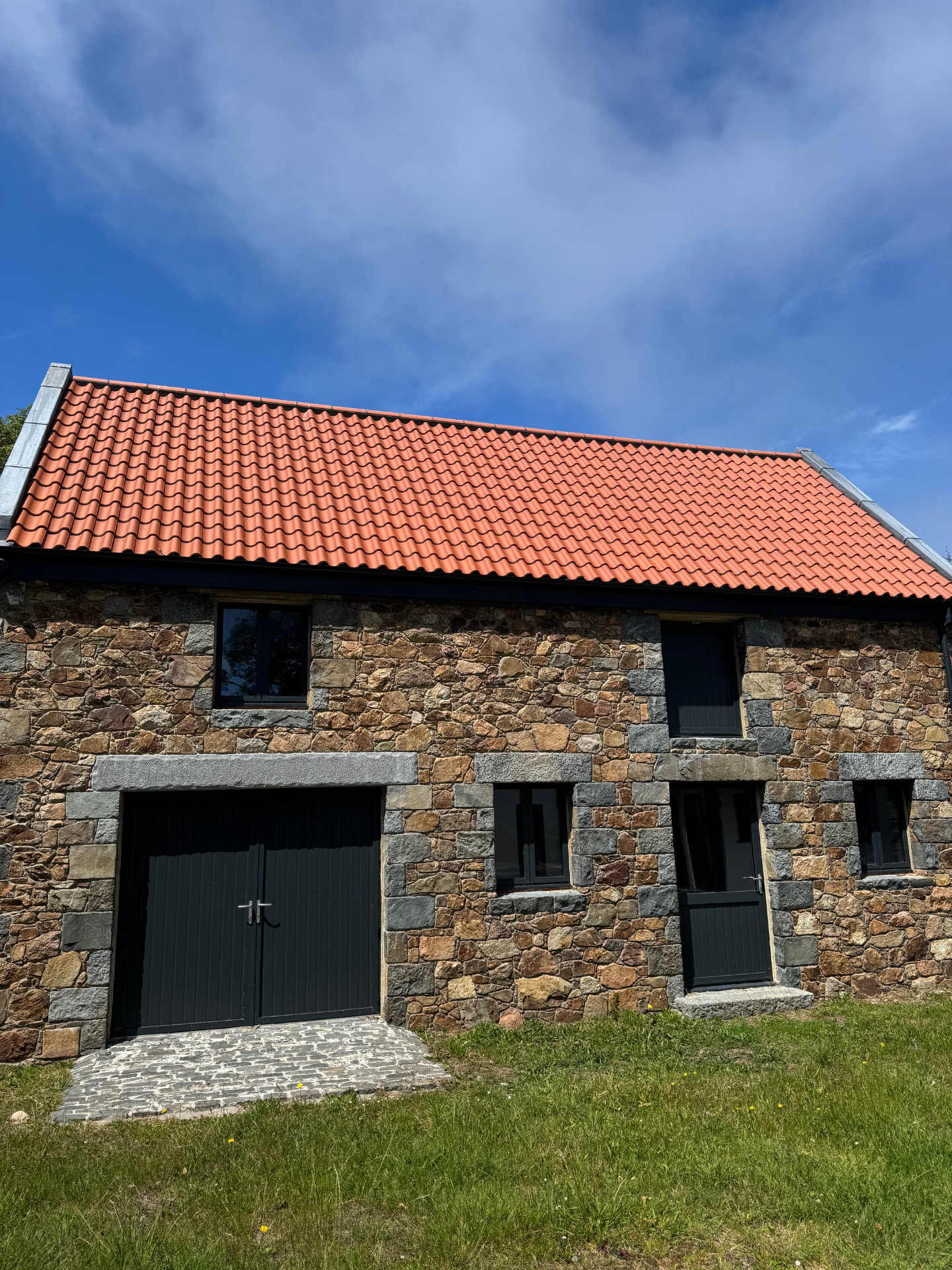 Restored stone barn with new red tiled roof, dark timber doors and black windows